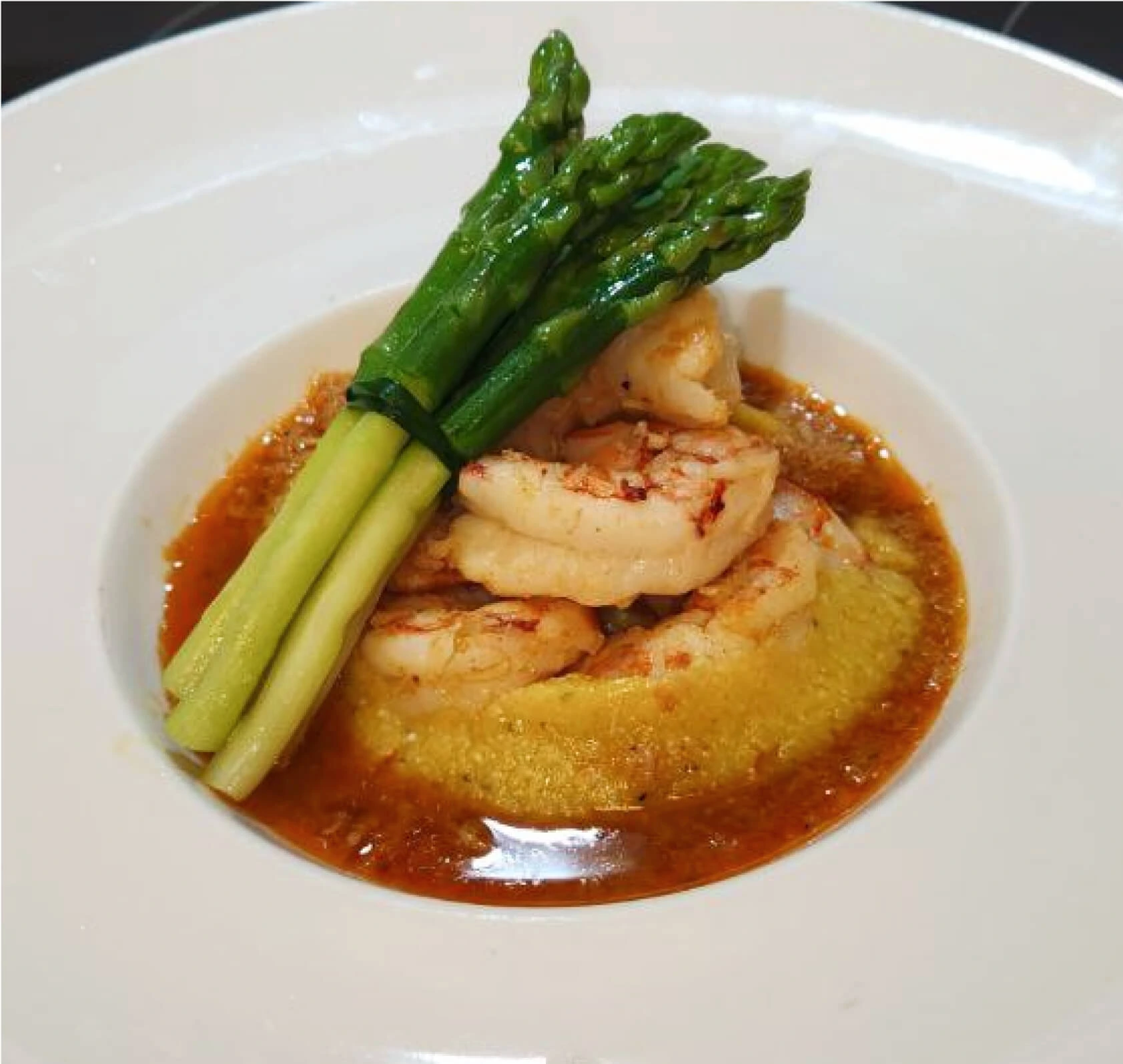 A bowl of cooked cornmeal showcasing shrimp and asparagus